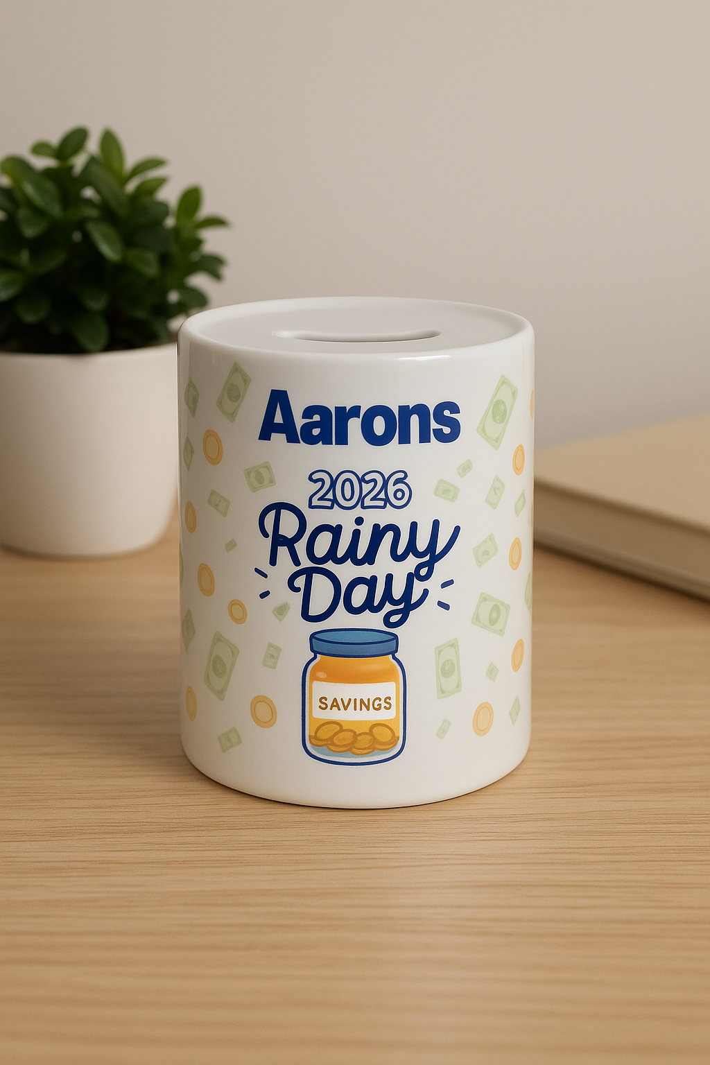 White ceramic container with 'Aarons 2026 Rainy Day' text and savings jar illustration on a wooden surface.